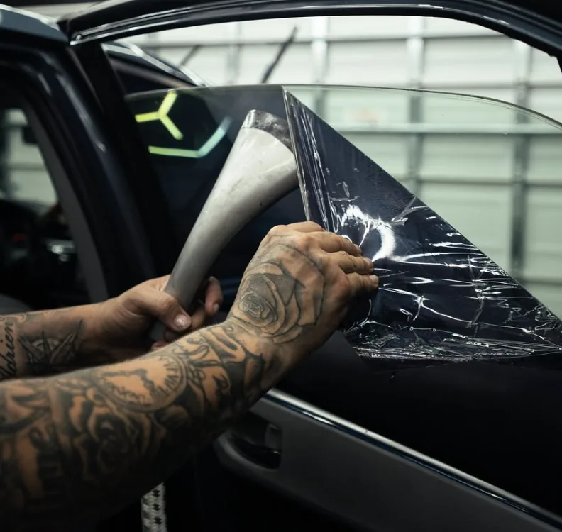 Hands fitting tint film on a car door window